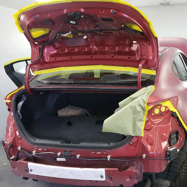 Red sedan masked and prepped in the bay before vinyl wrap film goes on