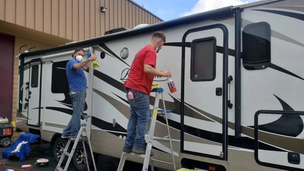 Two technicians cleaning and protecting a travel trailer's sidewall at Blue Rose Auto in Springfield, OR